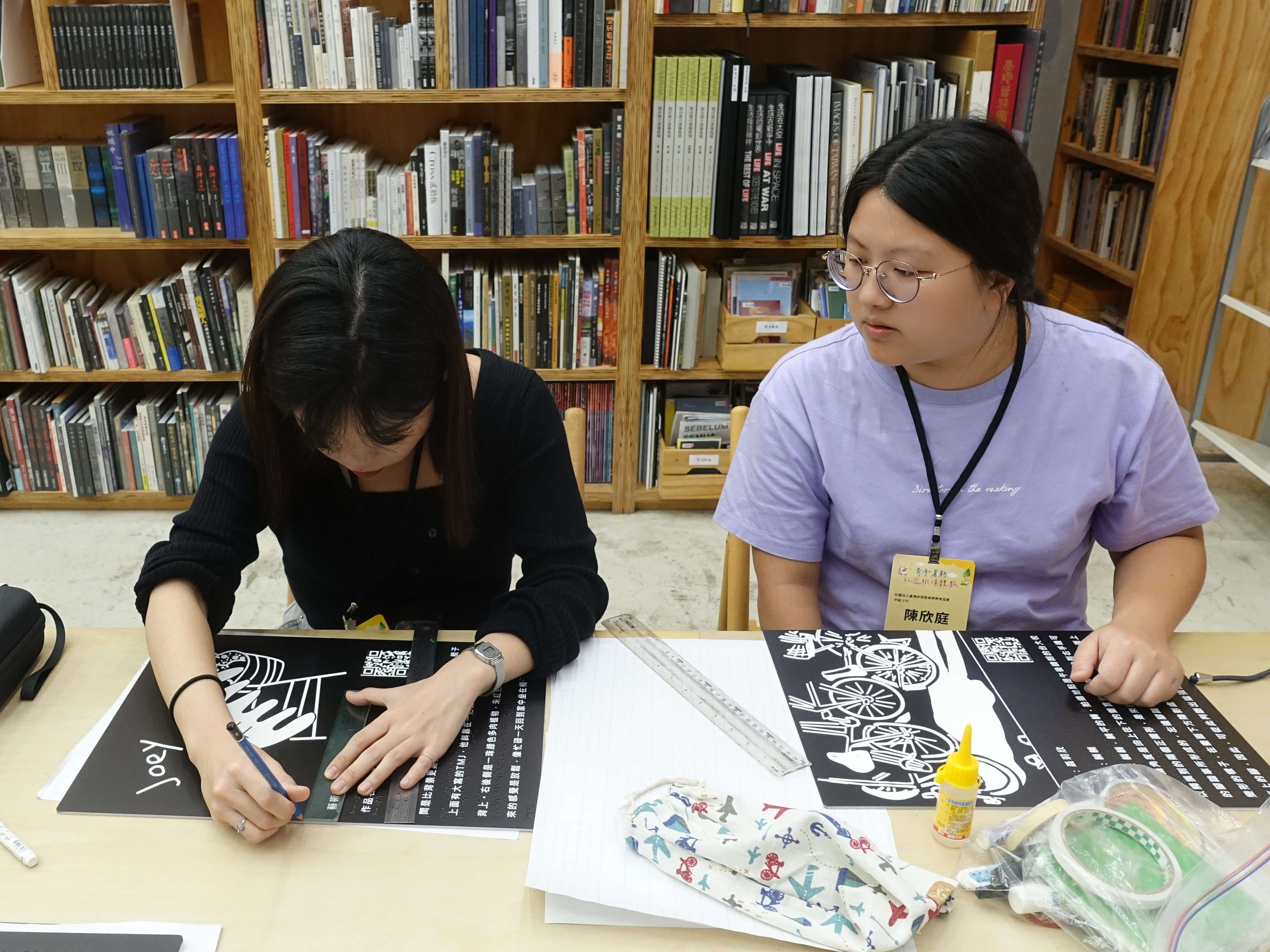 陳欣庭(右)與曹孟涵(左)製作展覽會之作品講解海報,含點字及語音導覽QR Code。