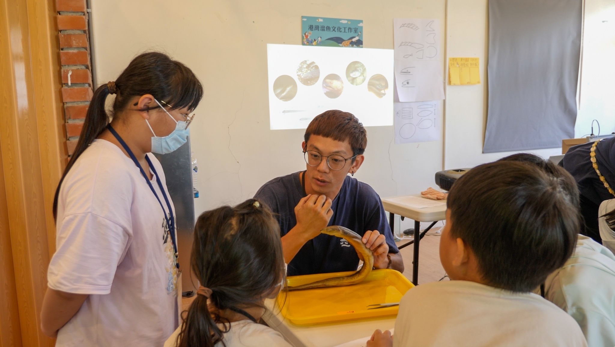 Team partner 俊傑 (Jun-Jie) teaches children to pay special attention to the differences in characteristics of fish when observing eels. (Provided by 港灣溜魚文化工作室)
